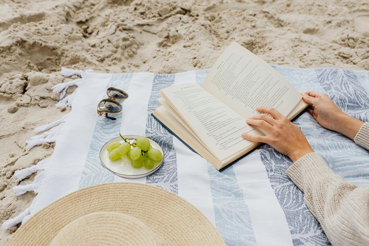 dłonie kobiety czytające książkę na plaży na kocu